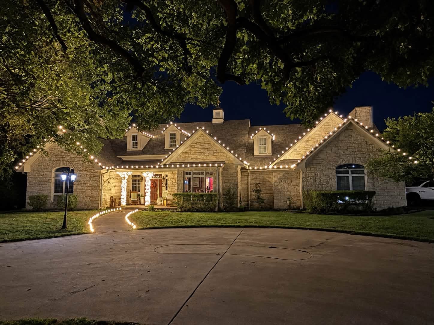 Warm white Christmas lights outlining a stone home and front walkway at night